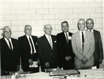 A group of men stand behind a table.