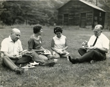 Four people seated on the grass eating.  Man on the far right is 'C. F. Dorsey'. 