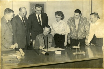 Mr. Hunter J. Conrad, Assistant Principal of Morgantown High School till 1963, is standing directly behind the man signing the document.
