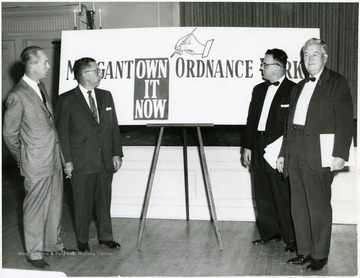 Four men standing near the sign to promote the selling of Morgantown Ordnance Works. 