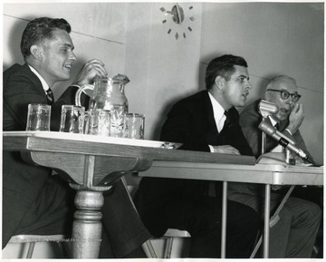 Three men seated at a table. The man in the center is Darrell V. McGraw, Special Assistant to Governor Hulett Smith.