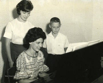 A piano teacher is giving a lesson to a young boy and girl.