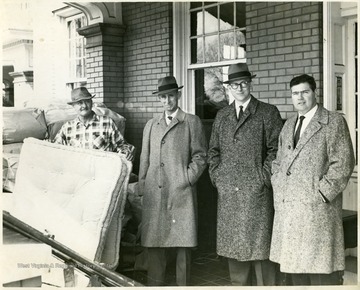 'County Commissioners J.D. Ward, Ken Kincaid and Tom Jackson' at the 'Sundale Rest Home reorganization day'. The men can be seen standing on the porch of the rest home among materials such as the mattress one is holding. Fourth man is unknown. 