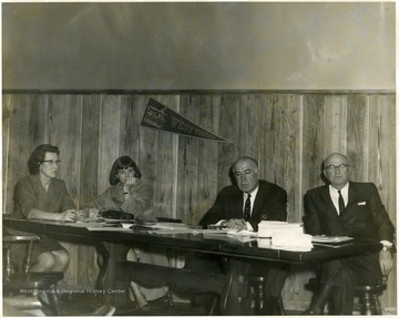 Two women, two men.  WVU pennant on the wall. Dyke Raese is the second from the right.