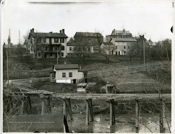 'South view of the late Judge Hagans' and Prof. Emery's residents, showing the small frame house at the intersection. Also the M and K tressel and the old Presbyterian Church. Taken from the South Morgantown covered bridge where the concrete bridge on University Ave. now stands.'