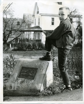 Young boy with a rifle poses next to the marker.  The marker, located at 305 Dewey Street, Morgantown, reads: 'This tablet marks the site of Fort Kerns erected at the beginning of Dunmore's War, 1774. Placed by the Elizabeth Ludington Hagans Chapter Daughters of the American Revolution, 1927.