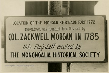 The sign reads 'Location of the Morgan Stockade Fort 1772 Morgantown was founded from this site by Col. Zackwell Morgan in 1785 this Flagstaff erected by The Monongalia Historical Society'.