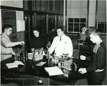 Teachers and pupils in University High School lab. At the time University High School was a division of West Virginia University for training teachers.  Pictured in the photograph are, from left to right:  Fred Truban, Carol Reynolds, Michael Caruso, and Scottie Riffle.  Girl in background unknown.