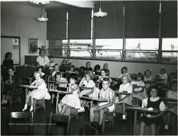 Teacher, Mrs. Eleanor Henry 'back left' and students sitting in the classroom.