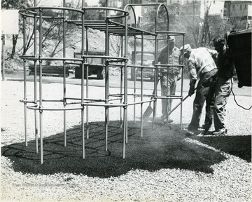 Three workers black top the playground at Central School.