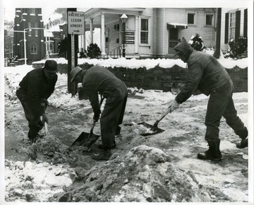 Three road crew members are shoveling a snowy sidewalk.