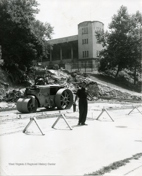 A flagman is directing traffic below the work area on Campus Drive.  West Virginia University stadium visible.