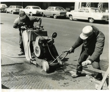 Two men working with equipment on a street in Morgantown.