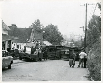 People watch as tow truck workers try to lift an overturned bus upright on Stewart Street in Morgantown, West Virginia.