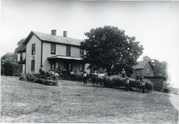 Farmers and horses standing out in front of a farm house.