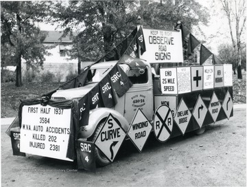 Truck covered with road signs and a posterboard listing the killed and injured from traffic accidents.