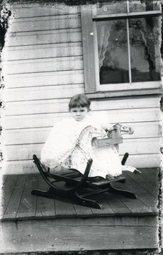 A little child in a rocker on a porch.