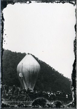 View of people gathered in a fenced field to view a hot air balloon rising into the sky in Morgantown, W. Va.