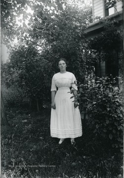 Woman standing next to bushes along a house.