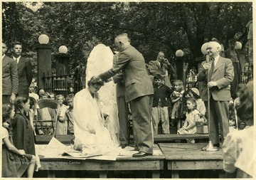 Queen kneels down as a man places a crown on her head.