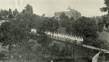 A scene of a group of girls standing on a bridge. Lincoln Cottage and grounds appear in the background.