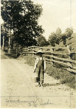 'Carrying a pail of eggs to Cottageville, the lad had a pail of fine, white eggs but he didn't know what kind of chickens produced them.' From photo album labeled 'Stewart A. Cody, County Agent, Jackson County, 1912.'