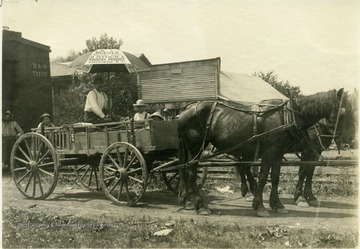 'A Country merchant with a load of poultry and eggs hauled several miles in the hot sun over rough country roads.'  From photo album labeled, 'Stewart A. Cody, County Agent, Jackson County, 1912.' Wording on umbrella says 'H. E. Beegle Wholesale Shipper of Country Produce, Ravenswood, W. Va.'  