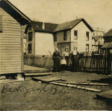 Three women and a child standing next to a fence in the back yard of the Hotel Stephenson.