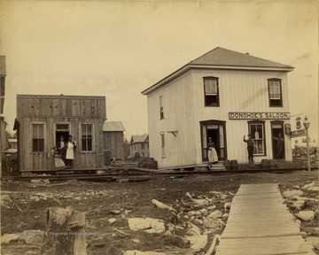 A view of Donohoe's Saloon in Tucker County. A residence is seen to the left of the saloon and people are standing outside on both porches.
