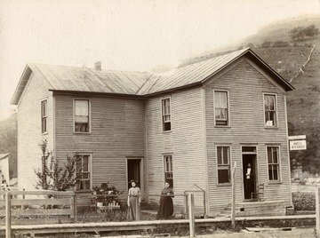 View of the Hotel W. H. Shobe in Laneville, West Virginia. Two women stand outside and a man stands in the entrance way.