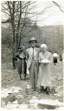 A photograph of Isaac Newton Ballard and Kate May Walkup Ballard standing next to a pile of what looks like plates and cups. Kate May Walkup ballard has a dish in her hands.