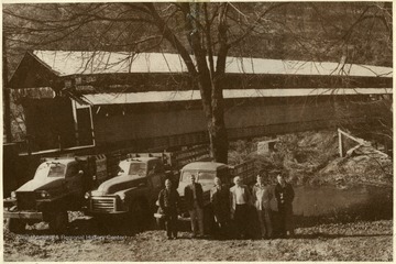 Six men stand near trucks by the covered bridge at Barrackville, W.Va.  The bridge was built in the fall of 1853.    