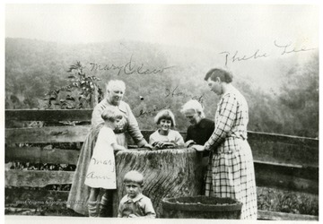 View of three women and three children standing by mortar in which George Hammer III pounded corn and other grain for his stock.  Pictured left to right- Mary Ann, Mary Claw, Grace, Hannah, Phebe Lee.