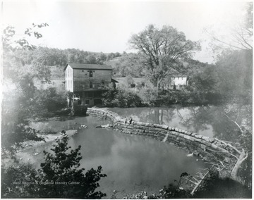'This dam was chartered one hundred years ago. The fifth dam was built on the site 1903-1904 by W. J. Moats. It is soapstone bottom and the water falling over the dam had cut a hole in the bottom which necessitated the curve at your right, the point in the middle is a pier. The stone in the burrhs came from France as ballast in empty ships, was built into burrhs by the Straub Machinery Company at Cincinnati, Ohio, served in the Harrisville Mill, then in the Henry Moats Mill on Addinson Run, now in the Mill at Rusk. They are still good for a hundred years. They were built for wheat but now grind corn and buckwheat. The wheat is ground on rolls. Many fossil fern and spruce branches are found in the soapstone under the mill. The third mill house is also on the site. There is a two mile swimming hole above the dam.'