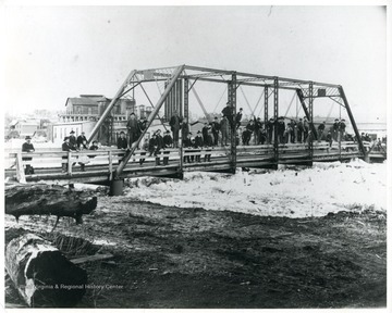A group of people have congregated on the bridge over the frozen river.