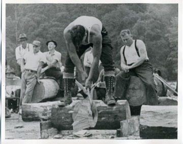 A man is participating in a chopping contest in Webster County, West Virginia, while others look on. 
