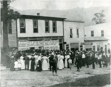 Group of people standing outside of Gillespie's Store during a sale.  Sign reads 'E. H. Gillespie's Entire $10,000 stock of high grade dependable merchandise to be turned loose at public sale beginning Wednesday, August 21st at 9 a.m. and lasting 10 days only.'