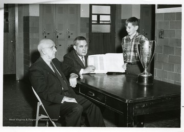 The Record Book Class as freshmen, 1967-1968, appreciated their heritage.  Left to right, Ex-principal C. H. Conway, Principal Robert G. Andrick holds the Record Book, David Gilkeson, president of freshman class. 