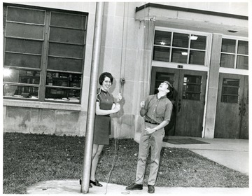 Record Book Presidents David Gilkeson (1967-68) and Barbara Tenney (1968-69) hoist the American Flag.  Barbara Tenney (Mrs. B. M. Cowger later on) was the Secretary of Student Council and David Gilkeson was the President of Student Council.