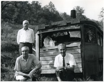 Three unidentified men pose in front of the old school bus.