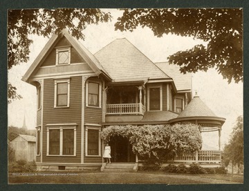 A lady is standing on the front steps of the J.W. Watson, Feetwell, Wilhelm House in Kingwood, West Virginia. 'J.W. Watson house, now owned by Feetwell, corner of Tunnelton Street in Kingwood. Home also of Judge Wilhelm in his later years.'