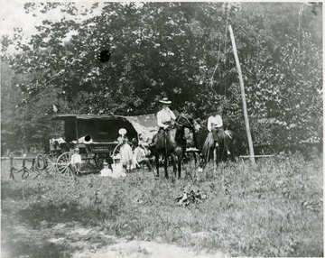 View of Man and lady on horse with children in background.  Sign on buggy reads 'T. A. Haldeman Vegetables'