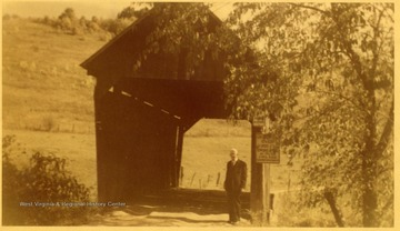 View of man standing at entrance of covered bridge.