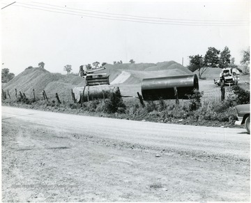 Photo includes earth moving equipment and piles of gravel and a tank of some sort.