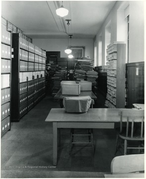 Books and paper in background. Boxes on the shelves on the left. Table and chairs in the foreground.