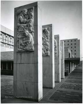 'The noted American sculptor Milton Horn was commissioned in 1954 to create a visual history of the healing arts for the proposed West Virginia University Medical Center. He produced eight panels in high relief, each three by seven feet, depicting important developments and personages in the history of medicine, dentistry, nursing and pharmacy. They are carved in white Georgia marble on each face of four 15-foot pylons at the entrance to the Health Sciences Center. For well over a year, the artist worked under a canvas canopy while his wife read from the Bible. People would come and watch and he would discuss politics, religion, or anything else; all the time, chiseling away and becoming quite a celebrity.'