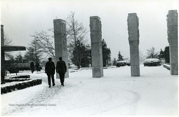 View of gentlemen walking by the pylons in front of the Medical Center on a snowy day.