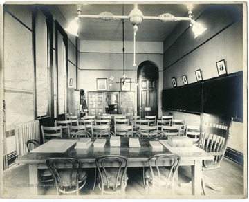 'Classroom in Woodburn Hall featuring gas lighting, blackboards, and standard furnishings.'