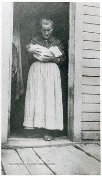 'Slavish [sic] mother stops her housework to be photographed with her six day old  baby.  Picture taken by District Nurse.' The mother is probably of Slavic origin. 