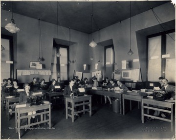 Students sitting at desks and tables using typewriters.